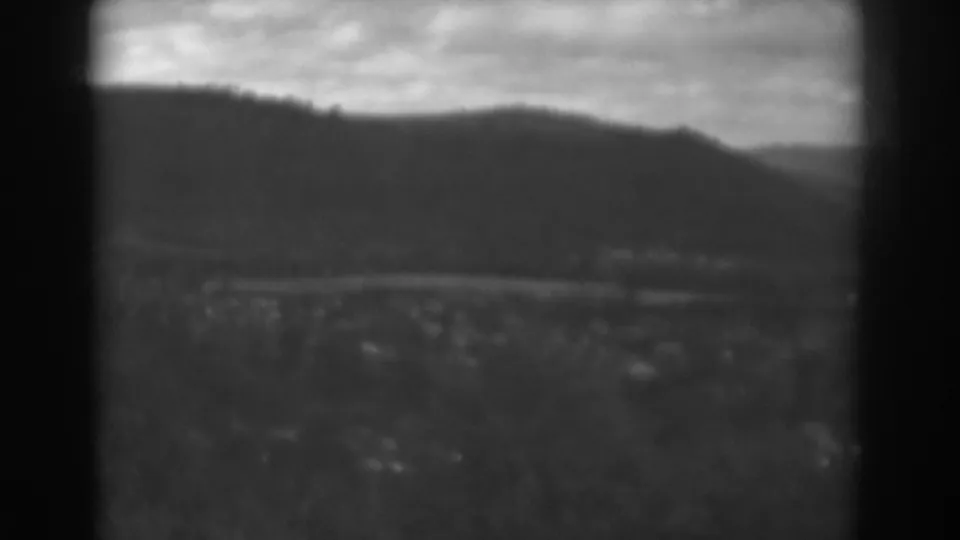 1938 Winchester, Maryland view with a dark vertical frame edge dividing mountains, cloudy sky, a distant road, and small buildings.