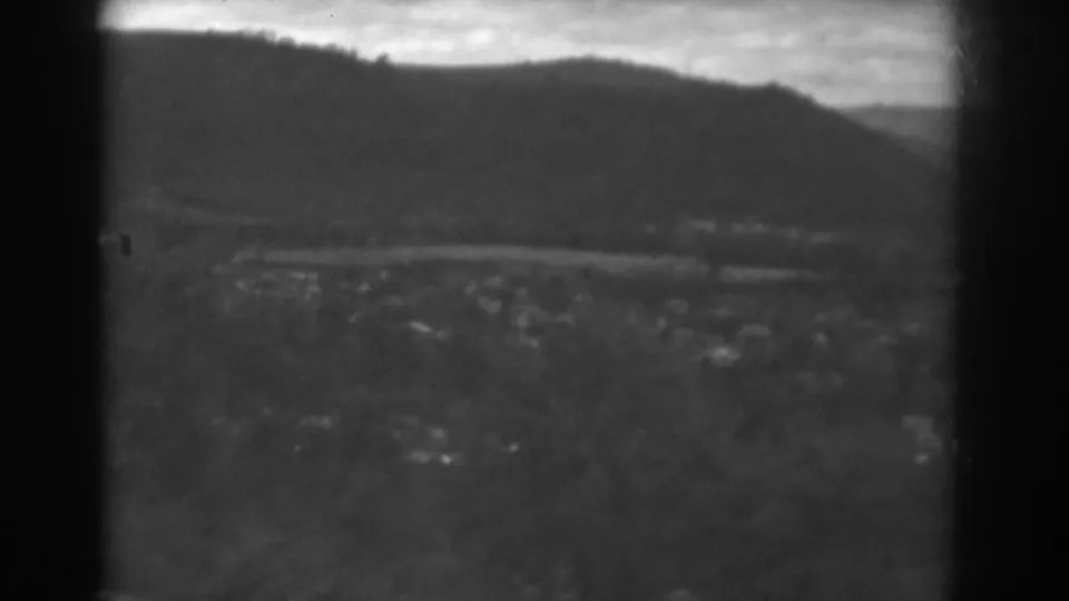 1938 Winchester, Maryland landscape seen through dark framing, with a road across the valley, scattered buildings, trees, and mountains.