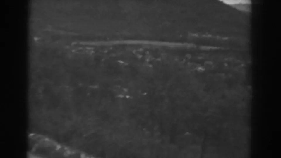 1938 Winchester, Maryland frame with foreground brush, distant buildings, a pale road, dark trim, mountains, and overcast sky.