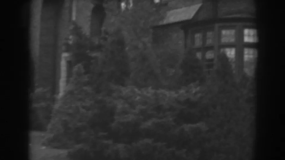1938 Winchester, Maryland home-movie view of a bay window partly hidden by shrubs and bare branches.