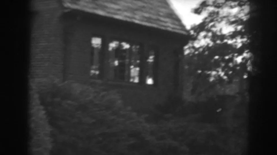1938 Winchester, Maryland frame showing the brick house side with windows, dark shrubs, and leafy branches at the right.