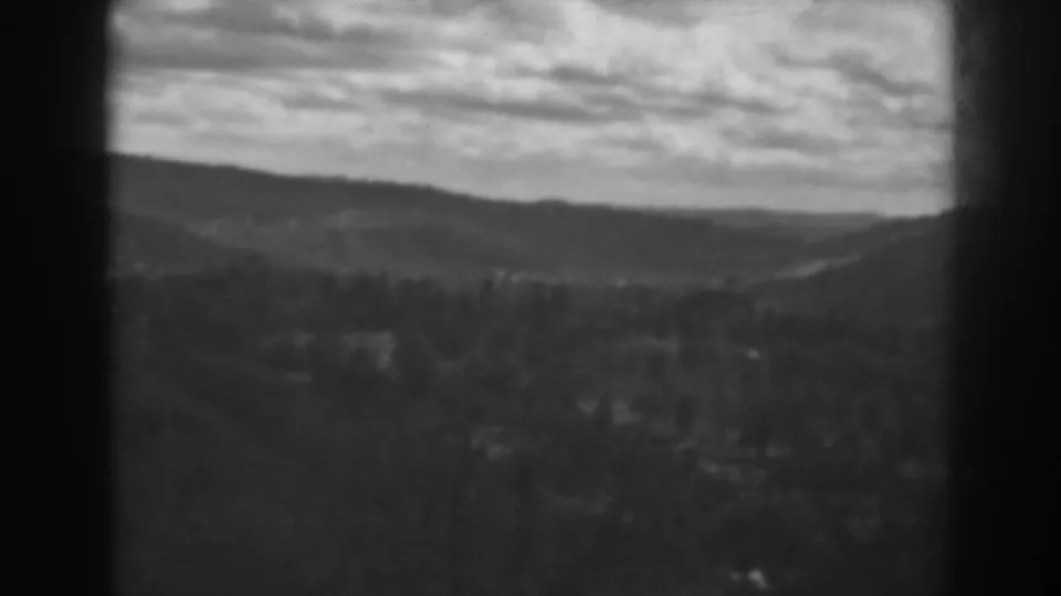 Wide 1938 home-movie landscape frame showing layered hills, a forested valley, and broad cloud cover in soft black-and-white film.
