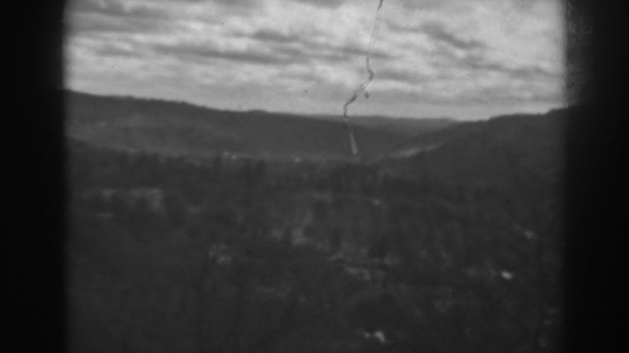 Soft black-and-white view of distant hills beneath a cloudy sky, framed by dark film borders.