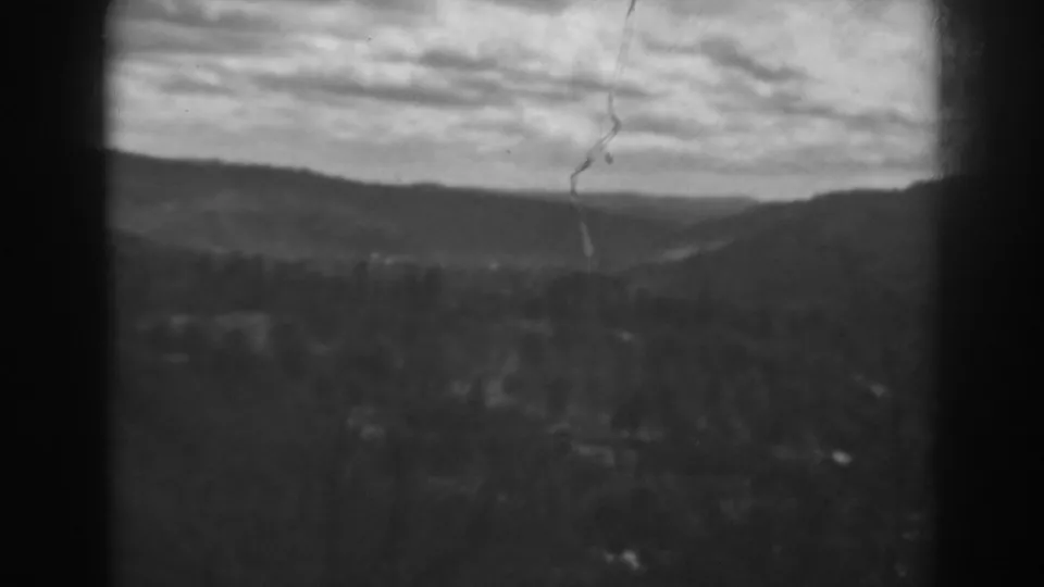 1938 8mm home-movie frame near Winchester, Maryland, showing hazy hills, low brush or trees, and a cloudy sky through dark gate edges.
