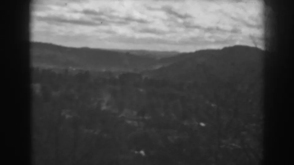 1938 8mm rural landscape frame showing a cloudy sky, distant hills, and shadowed trees or brush near Winchester, Maryland.