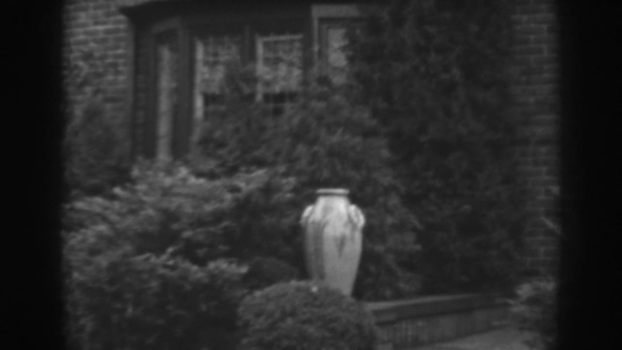 1938 Winchester, Maryland frame with a decorative urn centered against shrubs, vines, brickwork, and a multi-pane house window.