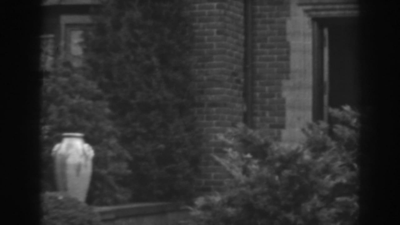 1938 8mm view in Winchester, Maryland, showing a brick and stone building entrance, shrubs, and a large decorative urn.