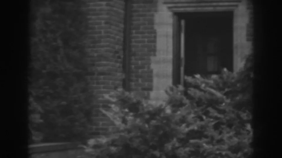 1938 Winchester, Maryland exterior detail with a stone-framed doorway or window set in brickwork behind thick bushes.