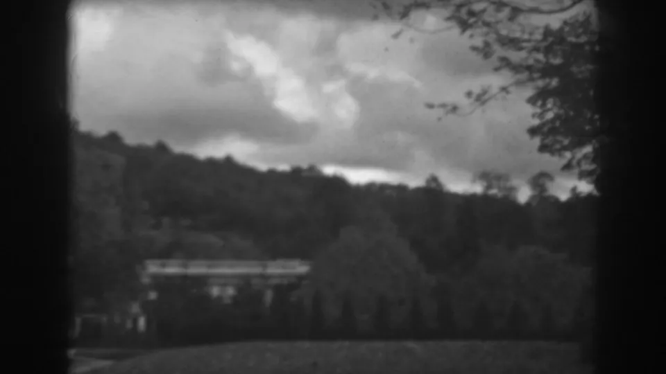 The view shifts to a wooded hillside near Winchester, Maryland, with a sloping lawn, tree line, and heavy clouds in 1938 8mm footage.