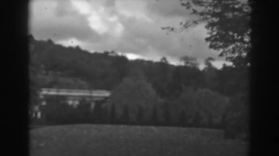 Late clip frame showing the same Winchester, Maryland hillside view, with cloudy sky, trees, lawn, and a distant structure softened by 8mm focus.