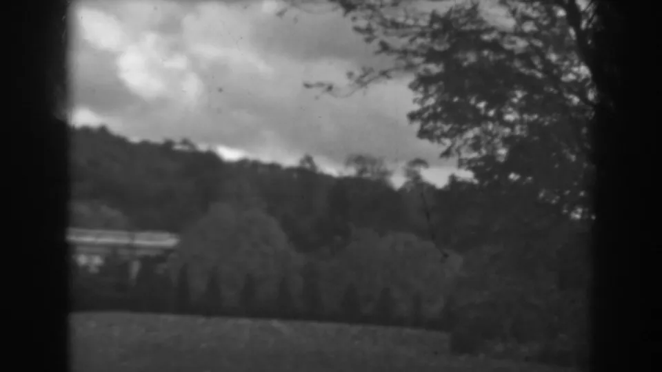 Soft 1938 home-movie frame from Winchester, Maryland showing clouds over a wooded hillside, trees in the middle ground, and grass in front.