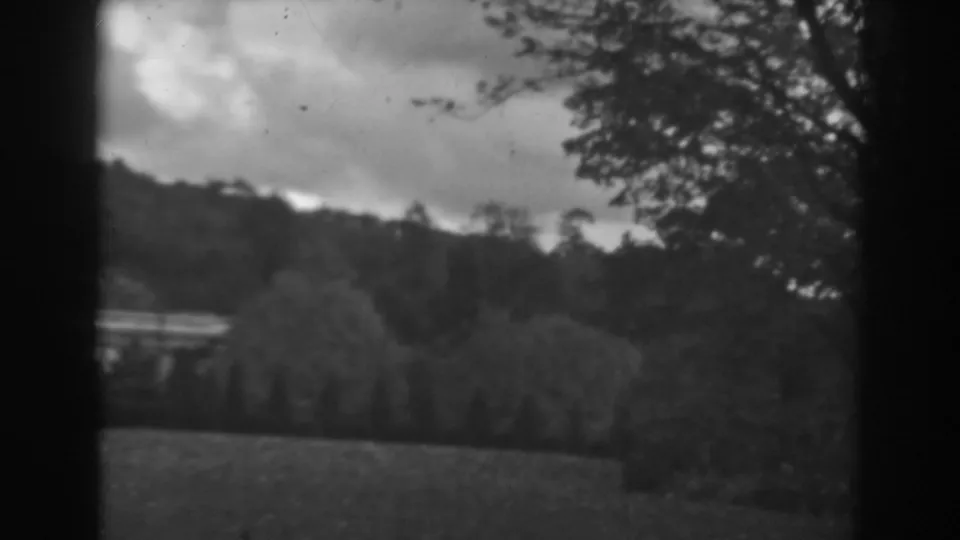 1938 Winchester, Maryland frame with a cloudy sky above a wooded hillside, leafy trees, grassy foreground, and dark 8mm borders at the sides.