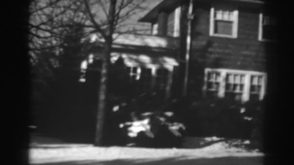 The camera continues across the Winchester house exterior, showing windows, winter trees, shrubs, and a parked car.