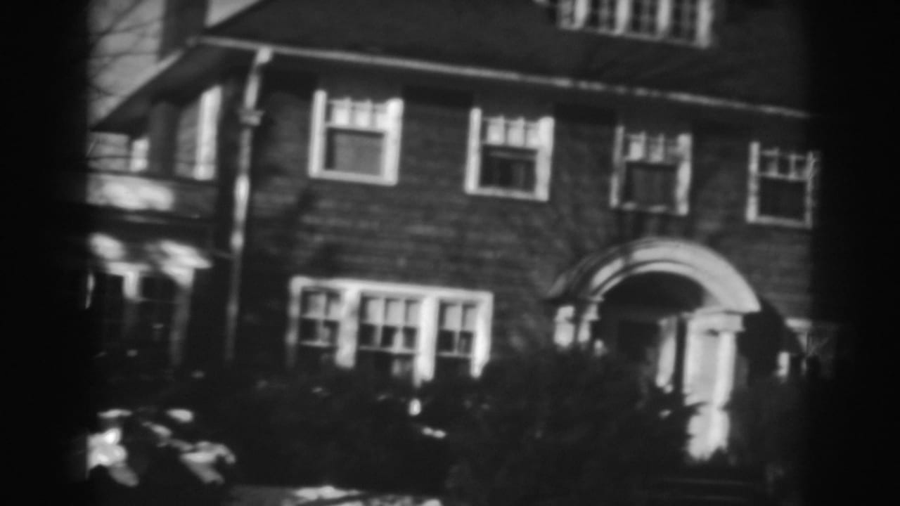 1938 Winchester, Maryland home-movie frame showing a brick residence, arched doorway, shrubs, bare trees, and light snow.