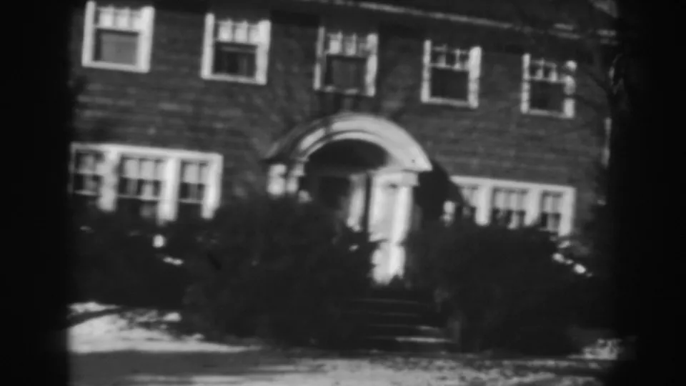 1938 Winchester, Maryland home-movie still showing the house facade, arched front entrance, shrubs, bare branches, and snow near the walkway.