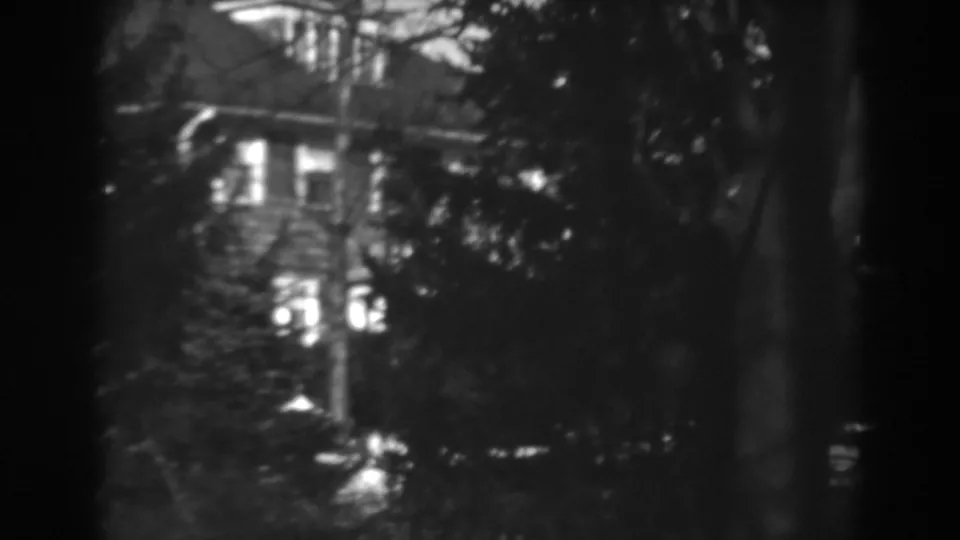1938 Winchester, Maryland 8mm frame showing a soft, high-contrast view of a house exterior through trees and shrubs.