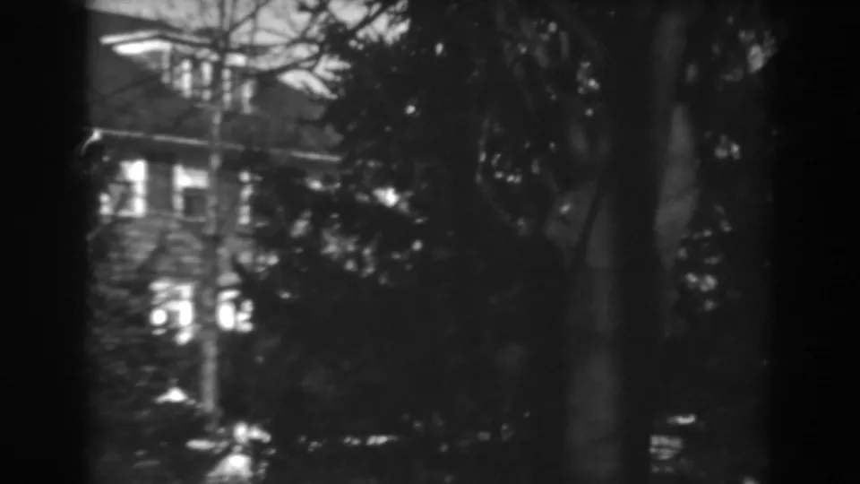 1938 Winchester, Maryland 8mm frame showing a large house behind tree cover, with windows glowing through deep shadow.