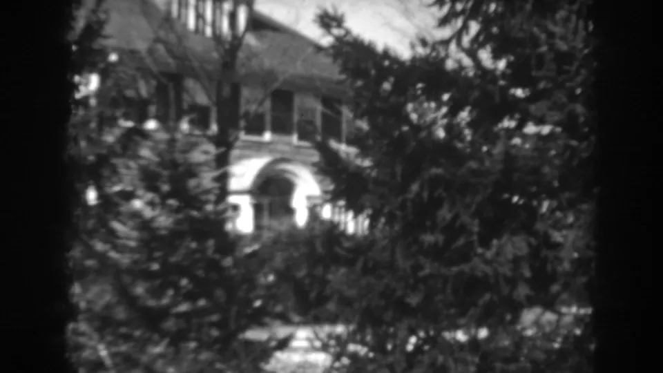 Home-movie still of a house front in Winchester, Maryland, with windows and an arched entry seen through trees.