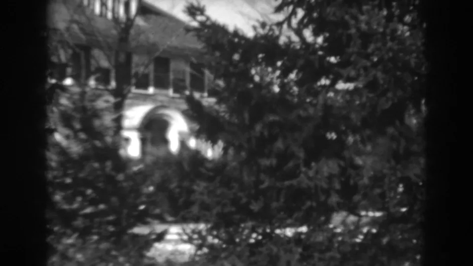 Late-1930s 8mm frame of a Winchester, Maryland residence partially hidden by trees and shrubs.