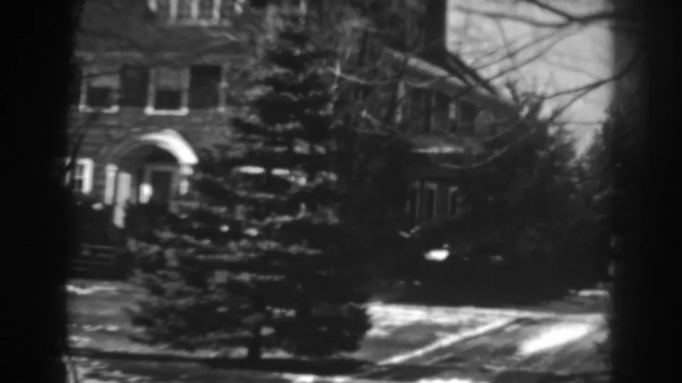 The house front remains centered, showing the arched entrance, symmetrical windows, evergreen trees, and winter snow patches.