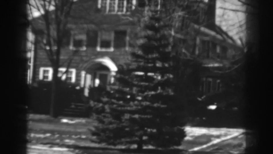 A closer winter view shows the brick residence, arched doorway, steps, windows, evergreen trees, and bare branches in soft 8mm focus.