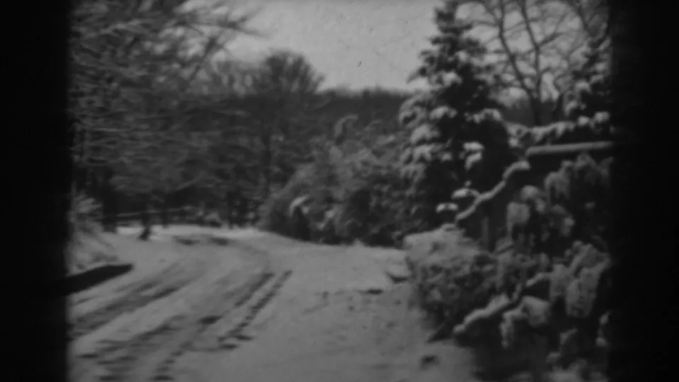 A snow-covered rural road with tire tracks curves through trees and shrubs in the 1938 Winchester, Maryland home-movie footage.