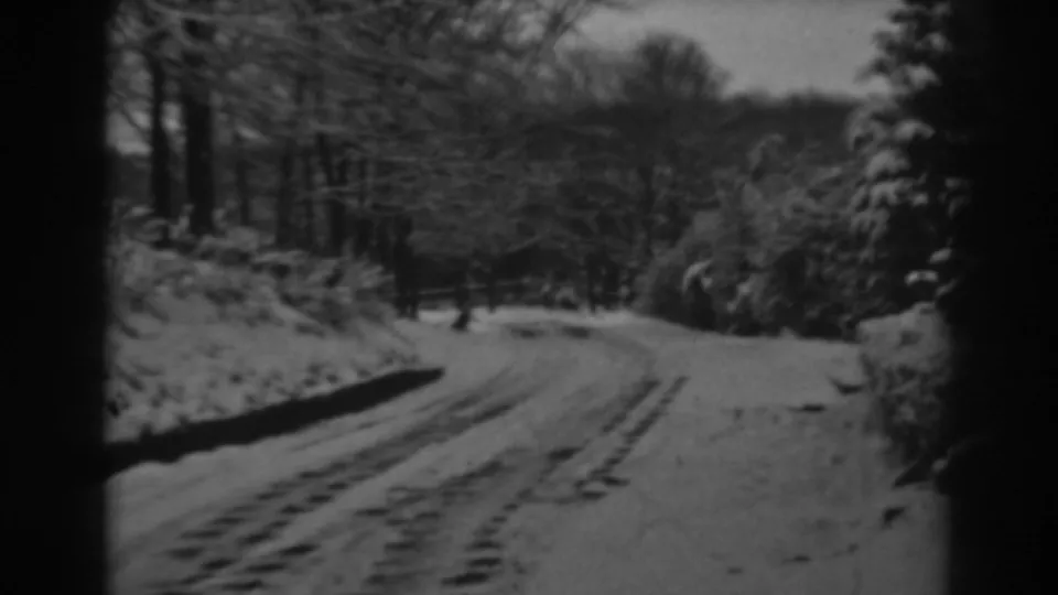 1938 8mm home-movie view of a snowy country road near Winchester, Maryland, with tire tracks and trees along the road edge.
