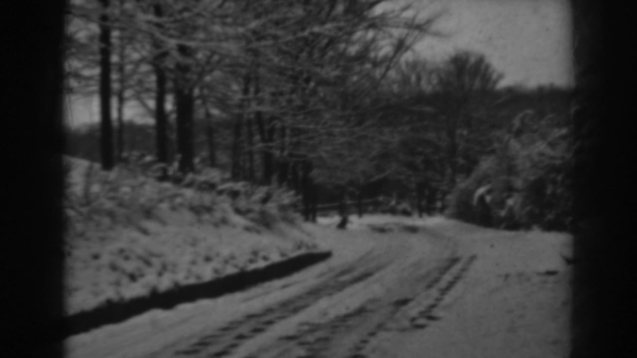 A snowy rural road appears from a moving 8mm viewpoint, bordered by bare trees and brush in Winchester, Maryland.