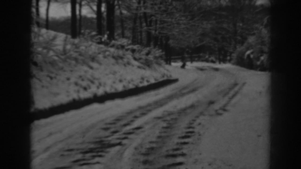 1938 8mm home-movie frame from Winchester, Maryland, showing a snow-covered rural road curving through winter woods.