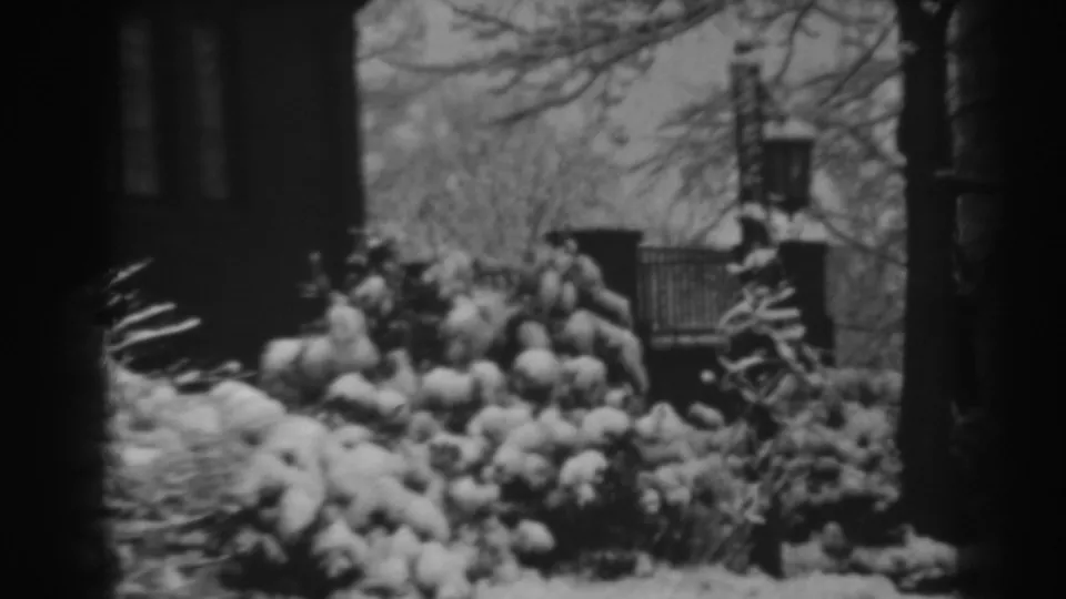 A snowy 1938 Winchester, Maryland residential exterior, showing bushes, bare trees, brick gateposts, iron fencing, and a large house beyond.