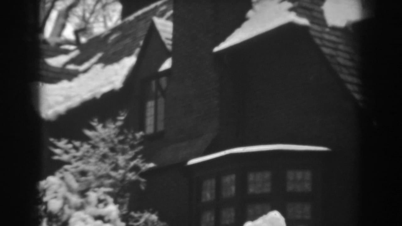 Winchester, Maryland home-movie frame of a snow-capped shingled roof, chimney and upper windows in winter light.