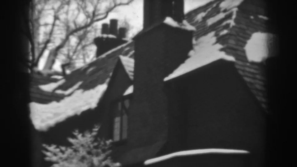 Late-frame view of the Winchester house roof, chimney and snow patches, bordered by dark 8mm frame shadows.