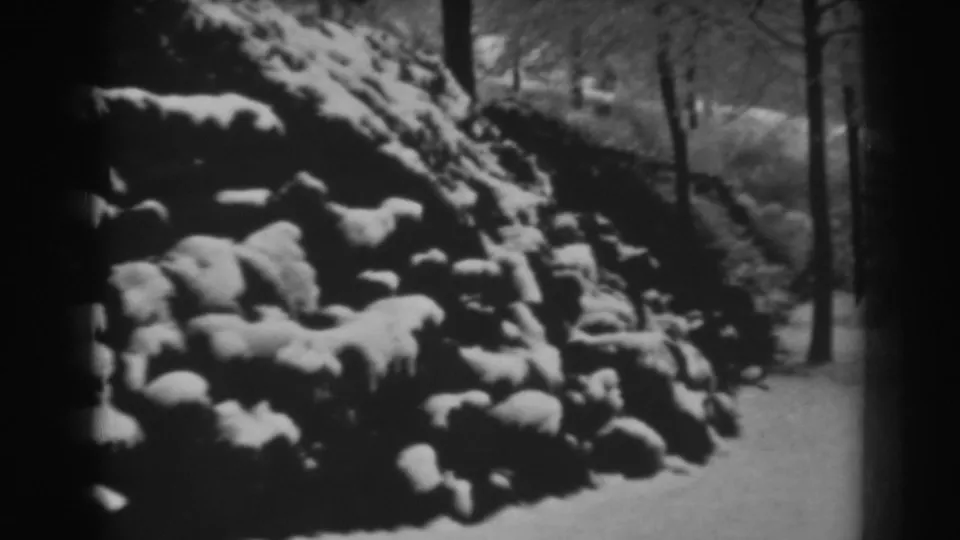 Closer 1938 8mm view of a snow-covered stone or earth formation with trees and winter ground nearby.