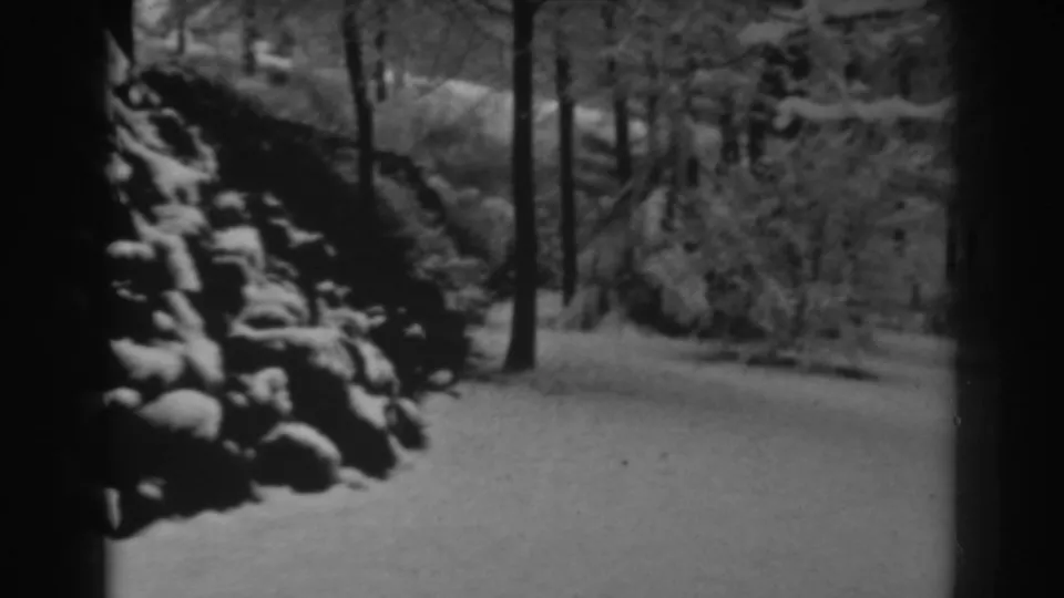 Home-movie frame of snow piled on rocks beside a wooded path, supported by metadata as Winchester, Maryland in 1938.