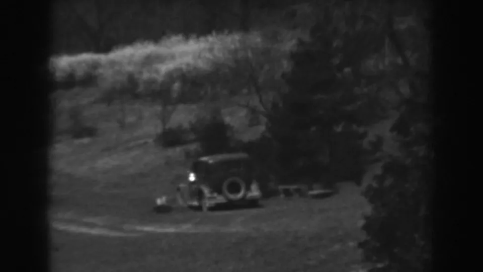 The parked car remains in view on the hillside, framed by dark trees and soft 8mm grain.