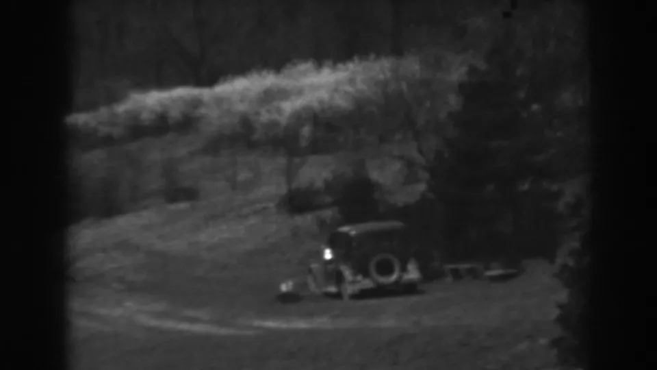 A parked 1930s car is seen from a distance beneath trees on a grassy Winchester, Maryland hillside.