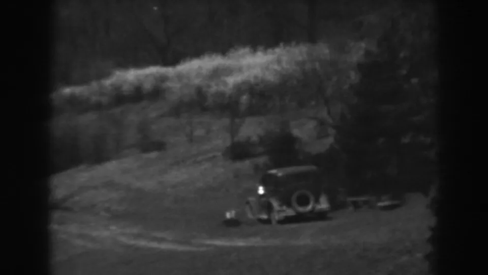 1938 Winchester, Maryland home-movie frame showing an early automobile on a grassy hillside near trees and a small wooden structure.
