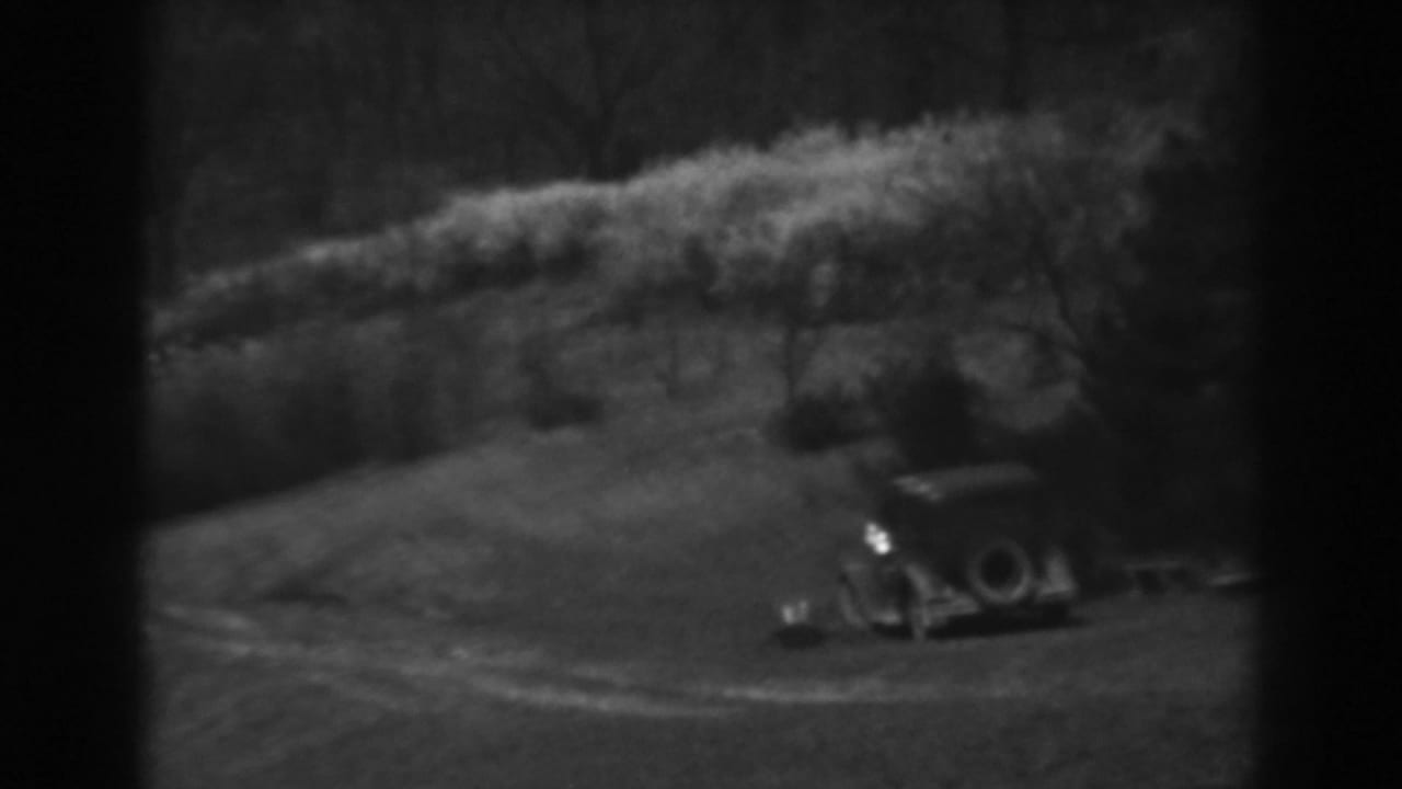 A soft black-and-white 8mm view of a parked early automobile and small structure in rural Winchester, Maryland, 1938.
