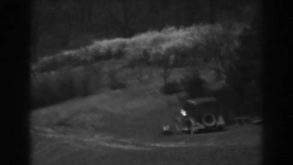 A soft black-and-white 8mm view of a parked early automobile and small structure in rural Winchester, Maryland, 1938.