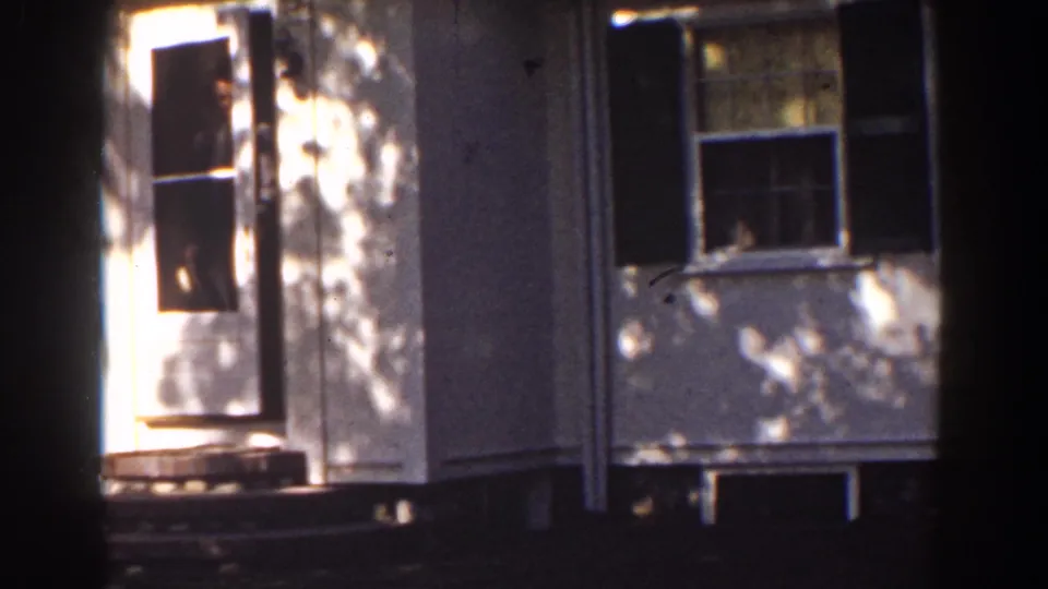 Adult man in dark clothing appears in the doorway of a white house in the Mount Washington, New Hampshire home-movie scene.