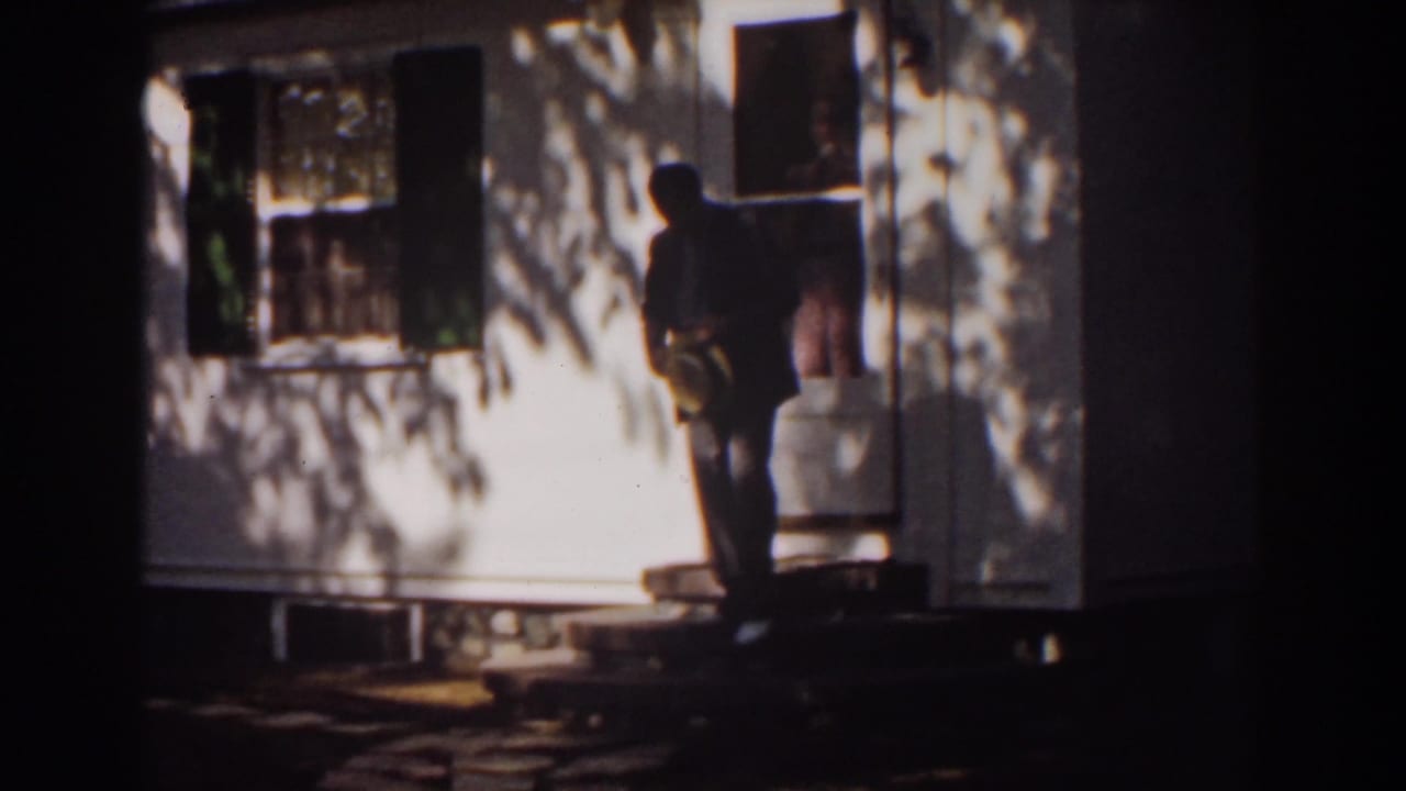 Man turns at the doorway of a white house with shadows across the siding.