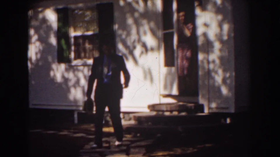 A suited man walks from the house while a woman stands in the doorway behind him in the supplied 1939 Mount Washington footage.