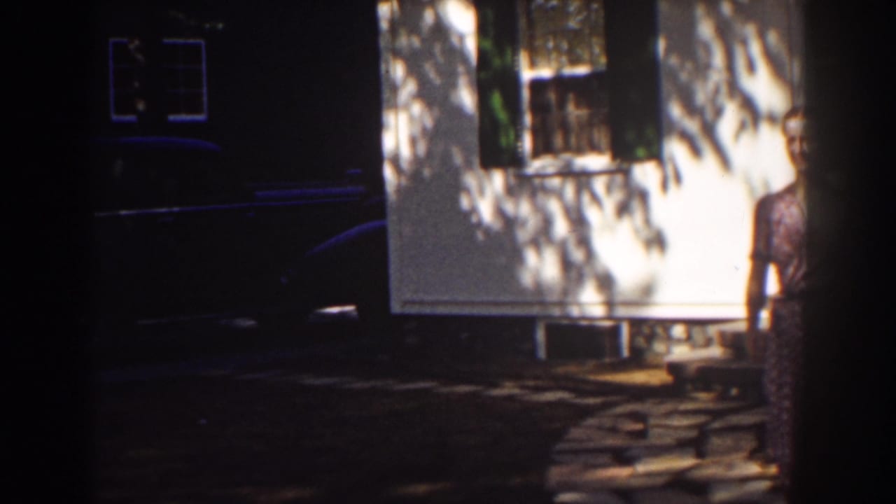 White clapboard house with shuttered window and a woman partly visible near the right edge.