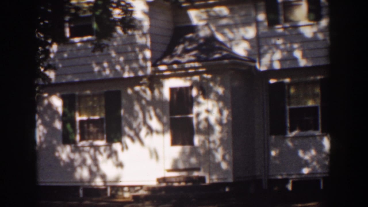1939 Mount Washington home-movie frame showing a white clapboard house with dark shutters and dappled tree shadows.