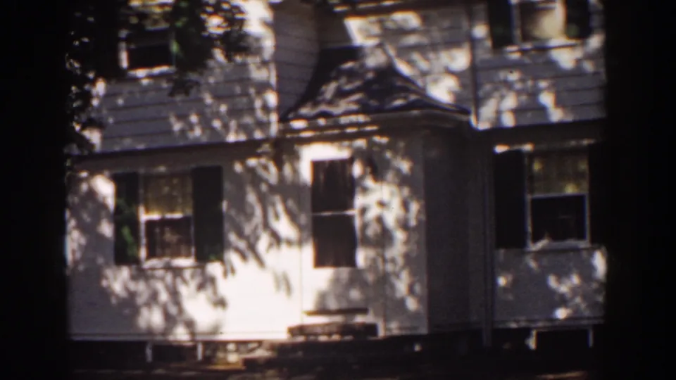 1939 Mount Washington home-movie frame showing a white clapboard house with dark shutters and dappled tree shadows.