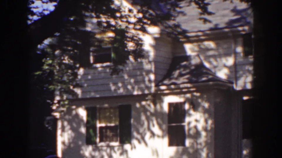 Late shot of the 1939 Mount Washington house exterior, with porch detail and shifting leaf shadows across the siding.