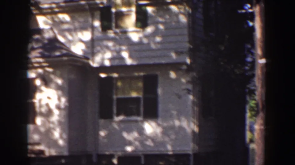 1939 home-movie view of a white residential exterior with shuttered windows and a large foreground tree.