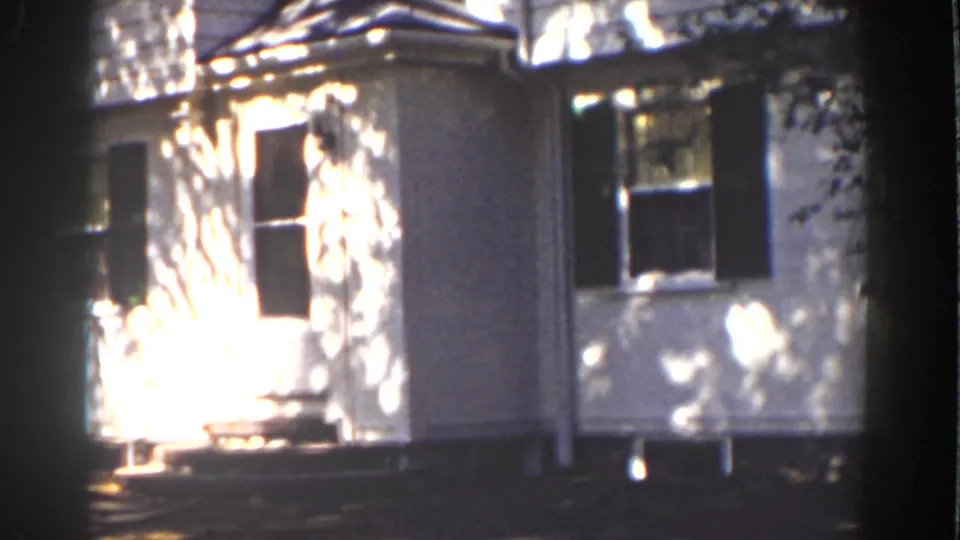 1939 Mount Washington frame showing a white house exterior with doorway, steps and shuttered windows in sun.