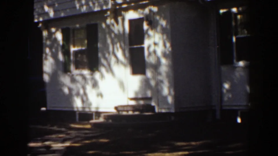 White two-story residential facade in Mount Washington, New Hampshire, framed from outside with strong sunlight and tree-shadow patterns.