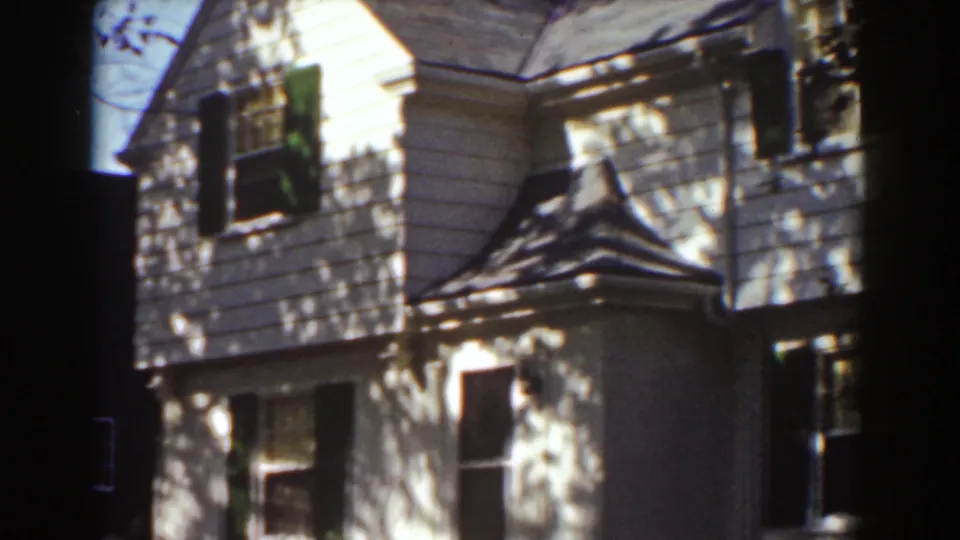 1939 Mount Washington home-movie frame showing a white clapboard house facade with dark shutters and dappled tree shadows.